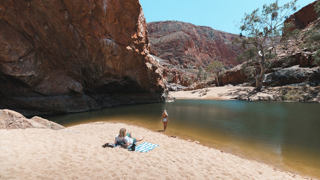 A couple relaxing on the sand by the waters edge at Ormiston Gorge