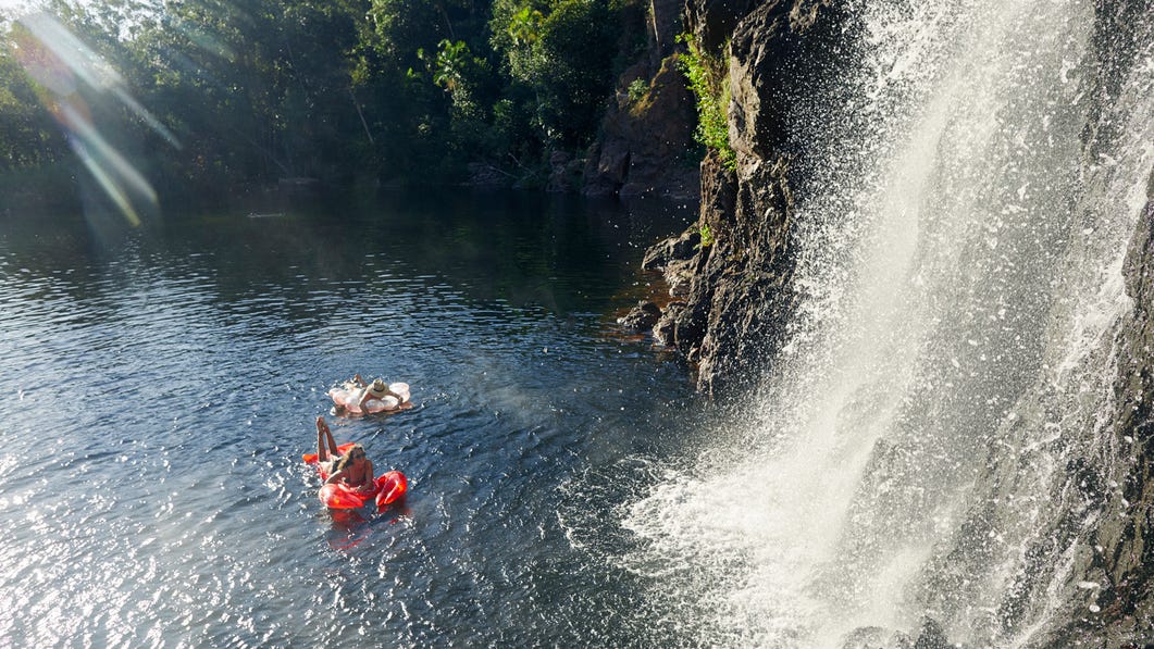 Two friends in the water in front of Wangi Falls floating on inflatables