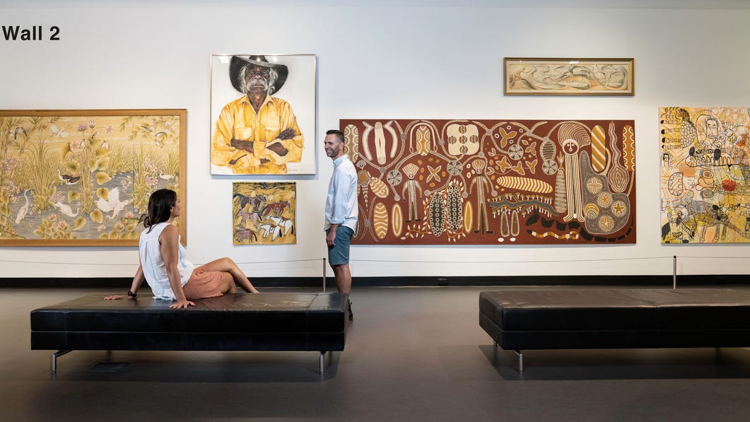 One woman sitting and one man standing looking at art
